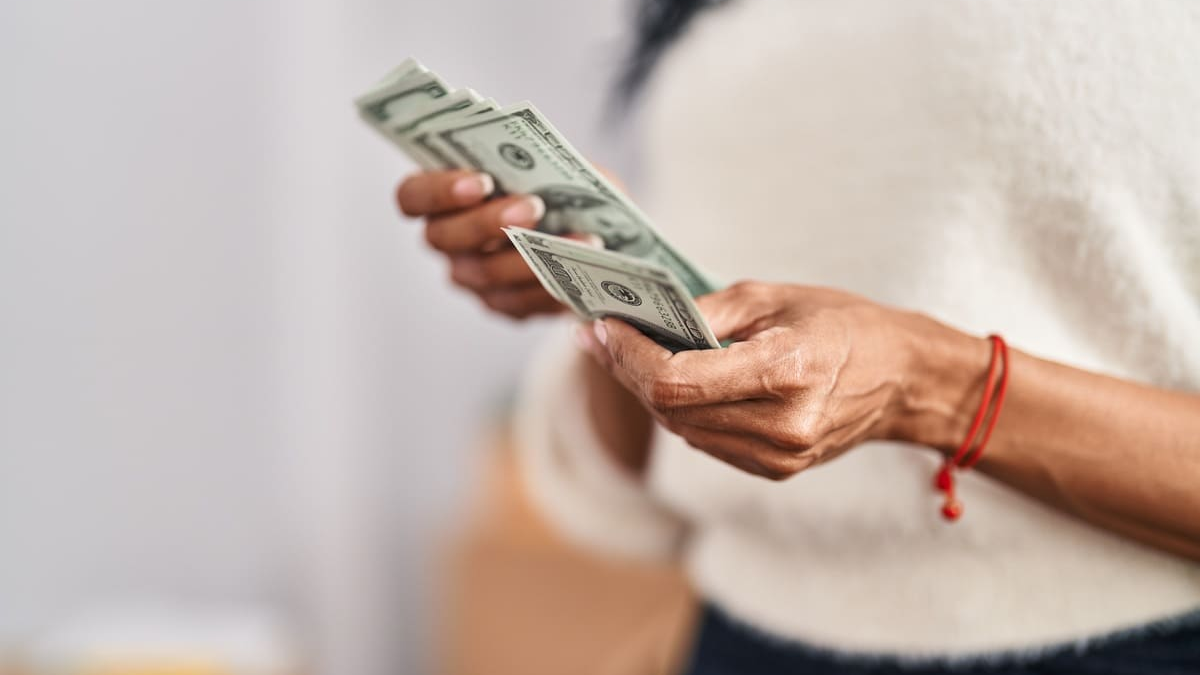 Pessoa segurando e contando notas de dinheiro. A cena transmite a ideia de alívio financeiro e reforço de renda, remetendo ao benefício do salário inss e à importância de administrar bem esse valor extra.