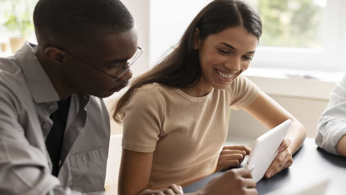 score conversa entre dois colegas analisando informações em um tablet, colaborando em uma mesa em um ambiente de escritório iluminado.