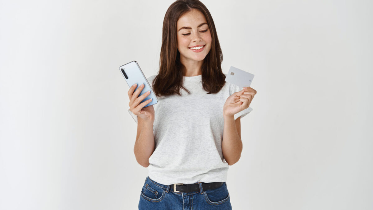 Jovem sorrindo, segurando um celular e um cartão de crédito Méliuz