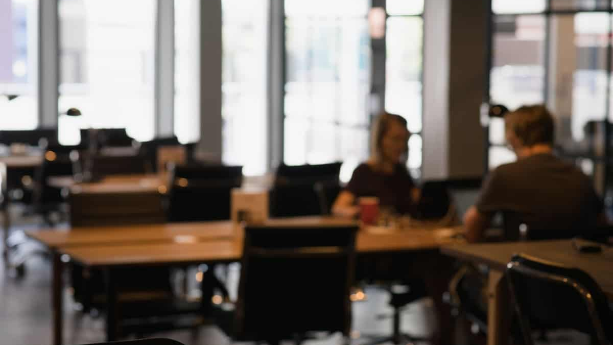 empréstimo para CLT ilustrado por ambiente de trabalho moderno, com mesas, cadeiras e pessoas conversando em um espaço corporativo, remetendo a contexto profissional e tomada de decisão financeira