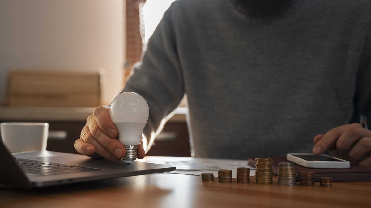 investimentos representados por uma pessoa organizando moedas sobre a mesa ao lado de um notebook e uma lâmpada, simbolizando planejamento financeiro, economia e tomada de decisões conscientes