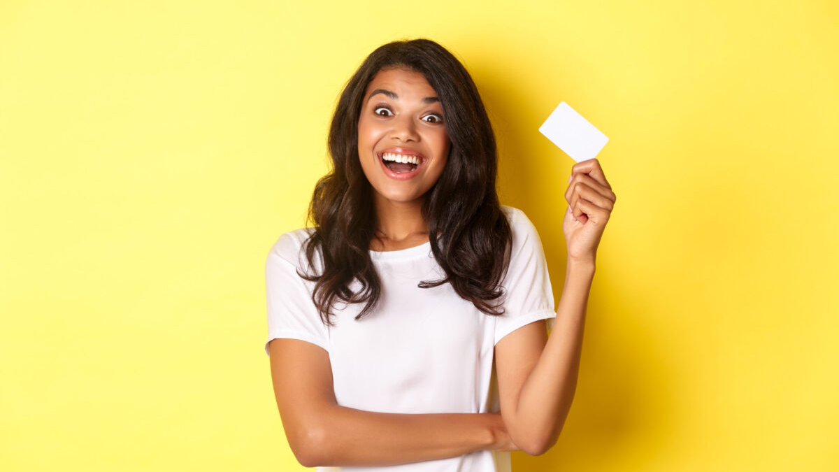 Jovem sorridente com blusa branca segurando um cartão de crédito.