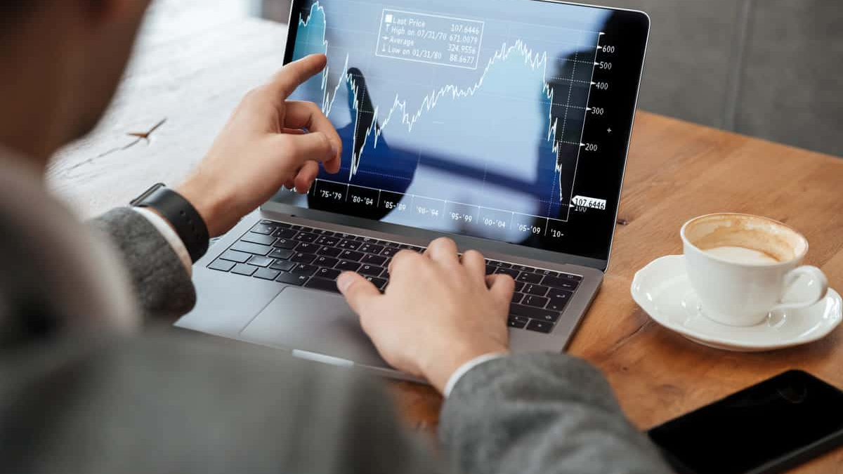 Pessoa analisando gráficos de investimentos em um notebook, apontando para a tela com atenção. A cena remete ao acompanhamento de aplicações financeiras e estratégias de rentabilidade, ilustrando o interesse em investimentos seguros como o Tesouro Direto.